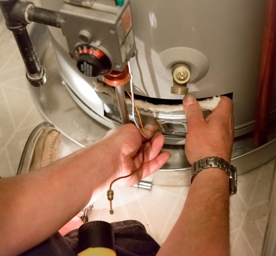 An image of someone taking off the access panel of a water heater, with the disconnected thermocouple sticking out