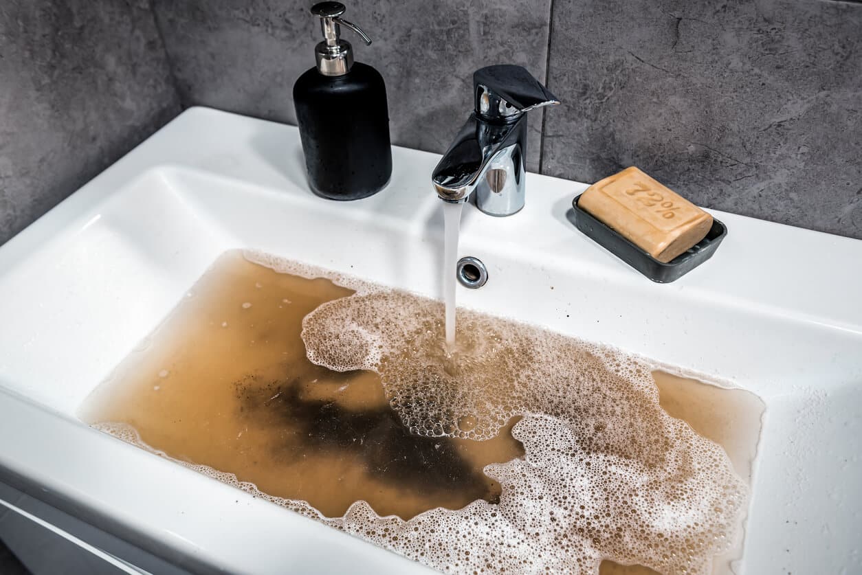 An image of a clogged bathroom sink, with dirty water and soap bubbles.