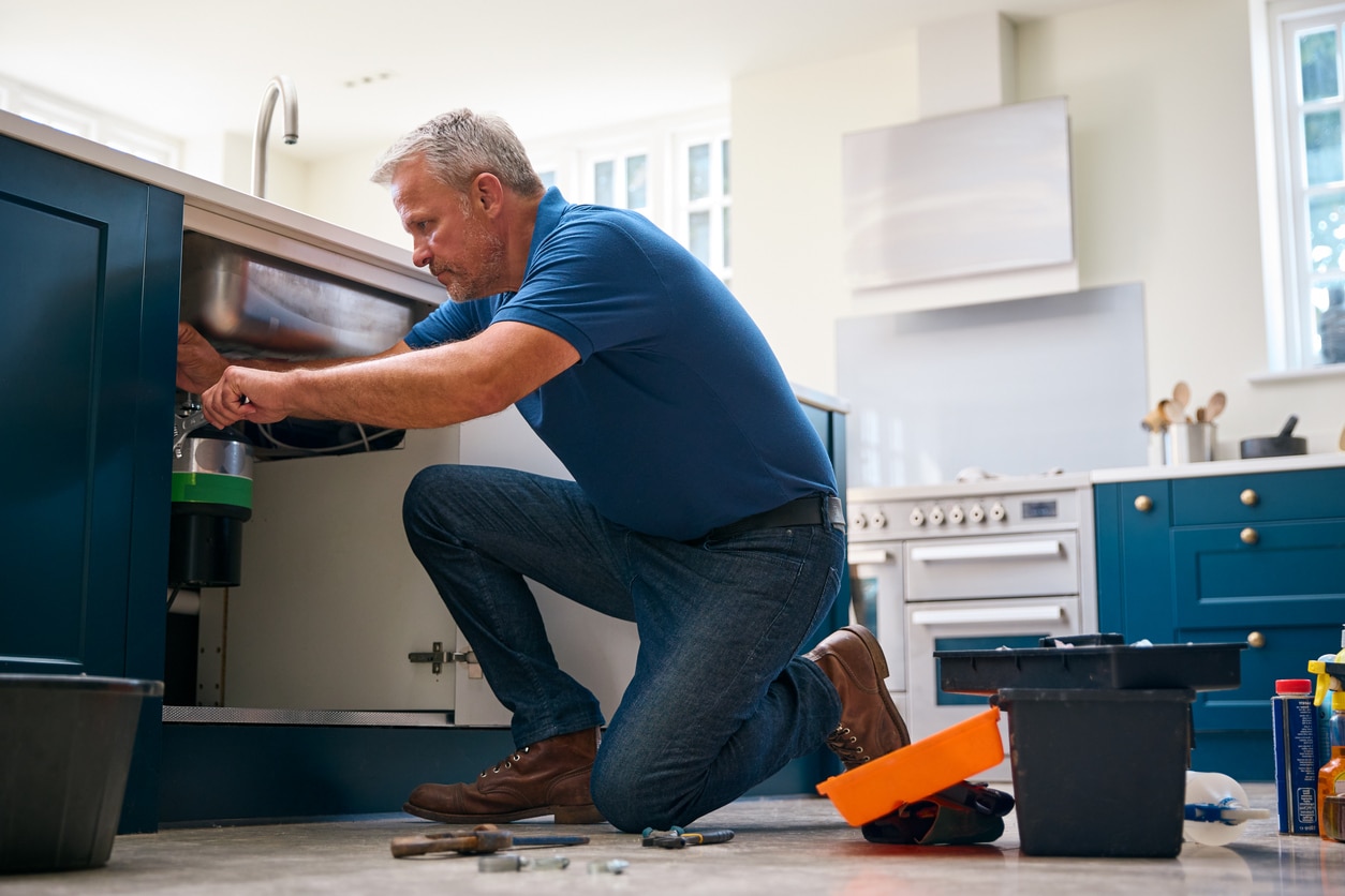 A plumber inspects and repairs a garbage disposal under a kitchen sink, providing expert service & reliable maintenance.